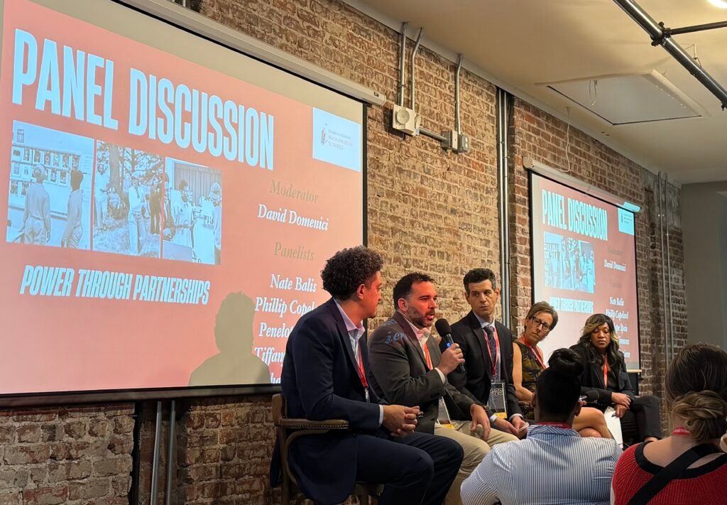 Speakers in front of a screen and brick background include Phillip Copeland, Michael Umpierre, Nate Balis, Penelope Spain, and Dr. Tiffany Simmons