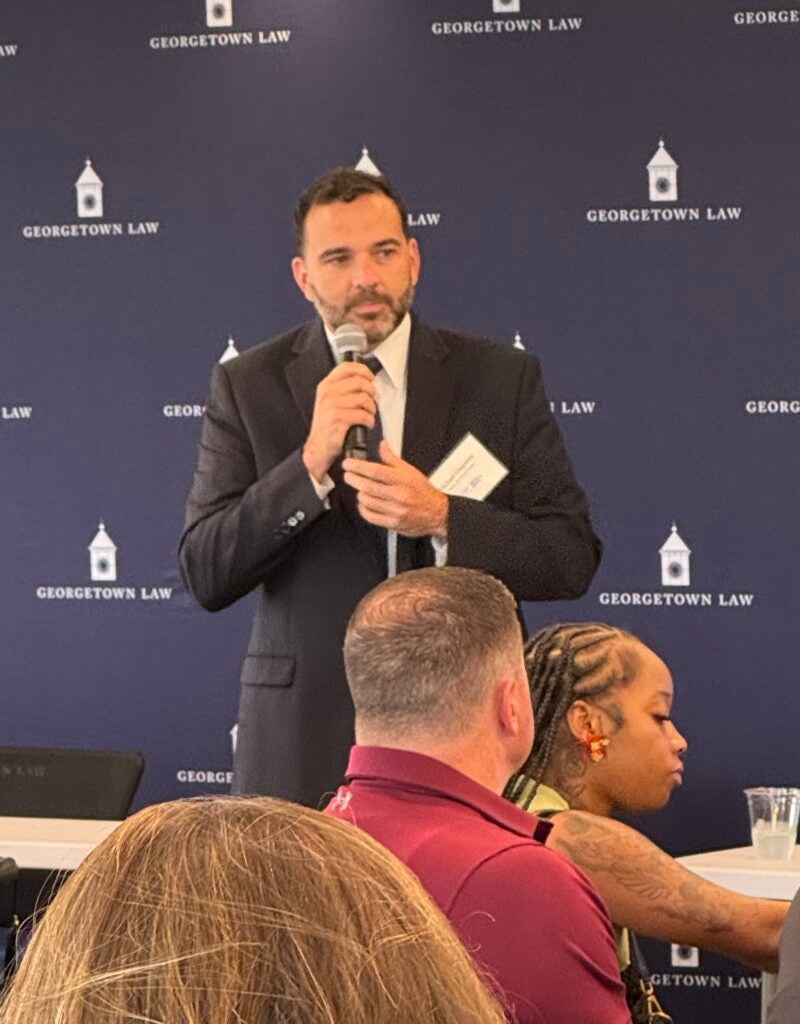 Michael Umpierre speaking in front of a Georgetown Law background in a room full of Certificate Program participants