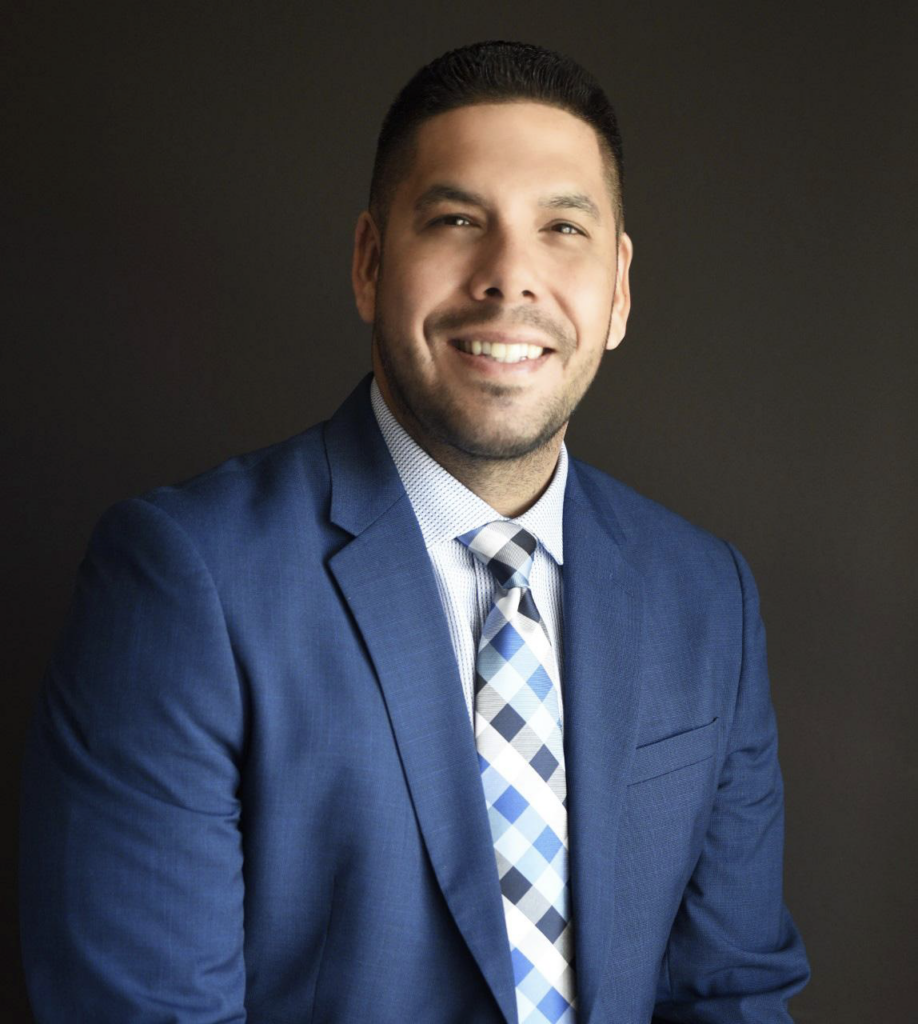 Photo of Ramon Ramos in suit and tie, smiling